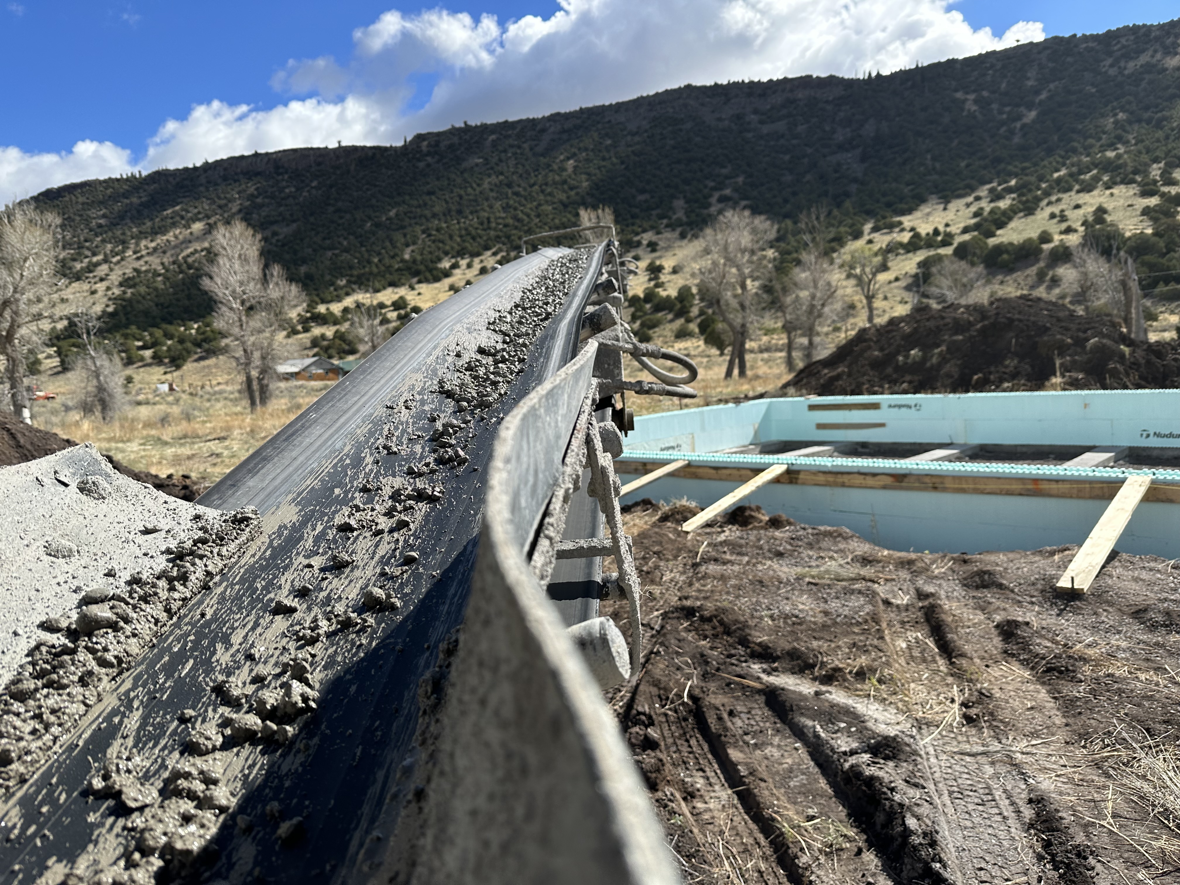 Conveyor belt placing concrete with mountain backdrop