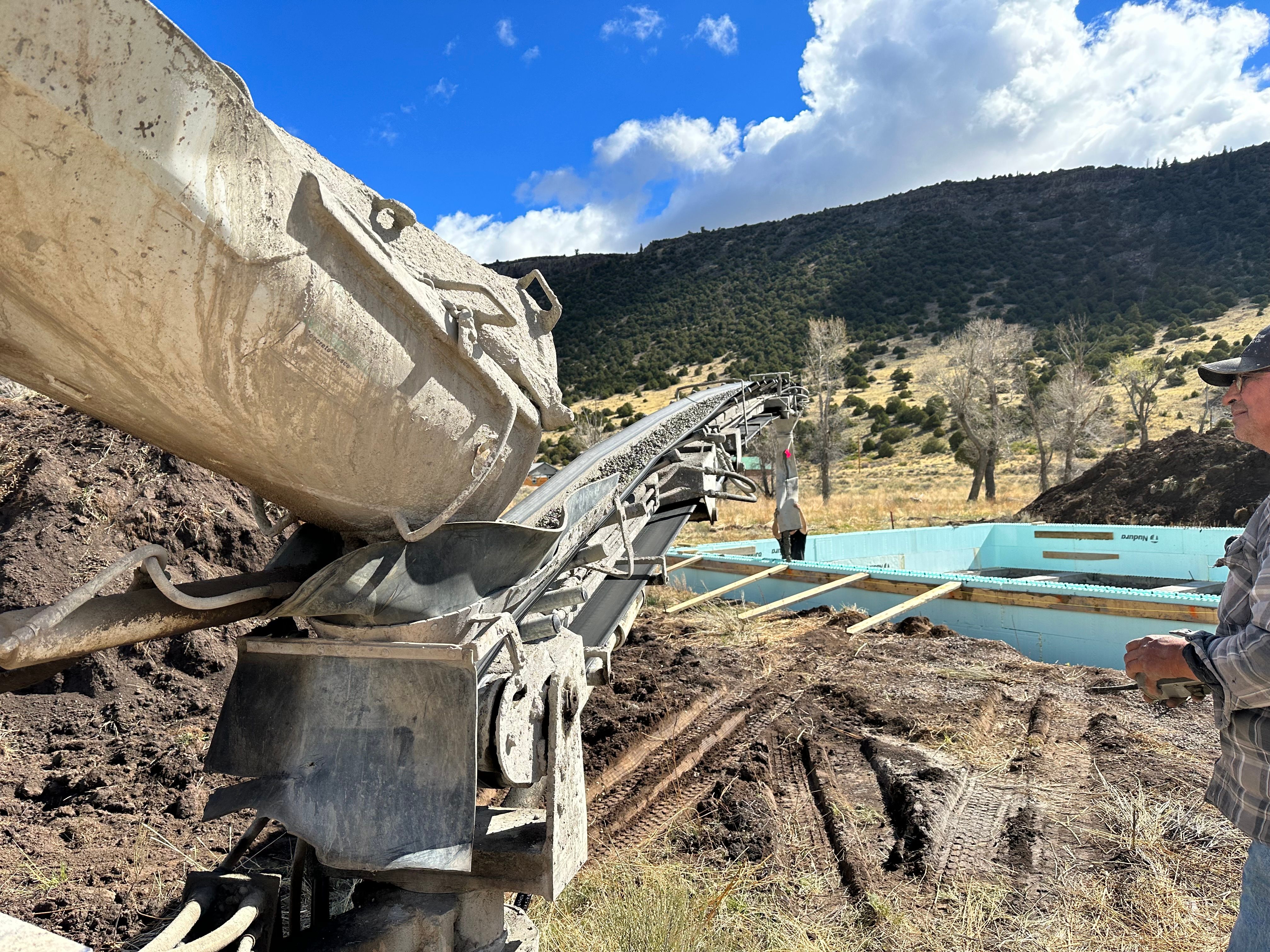 Mixer drum pouring onto conveyor belt at a foundation site